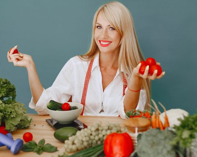 Healthy lifestyle concept with woman holding tomatoes and surrounded by fresh vegetables in a studio setting.