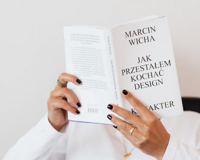Anonymous female in white shirt with gold chain on neck reading interesting book covering face while sitting on black chair